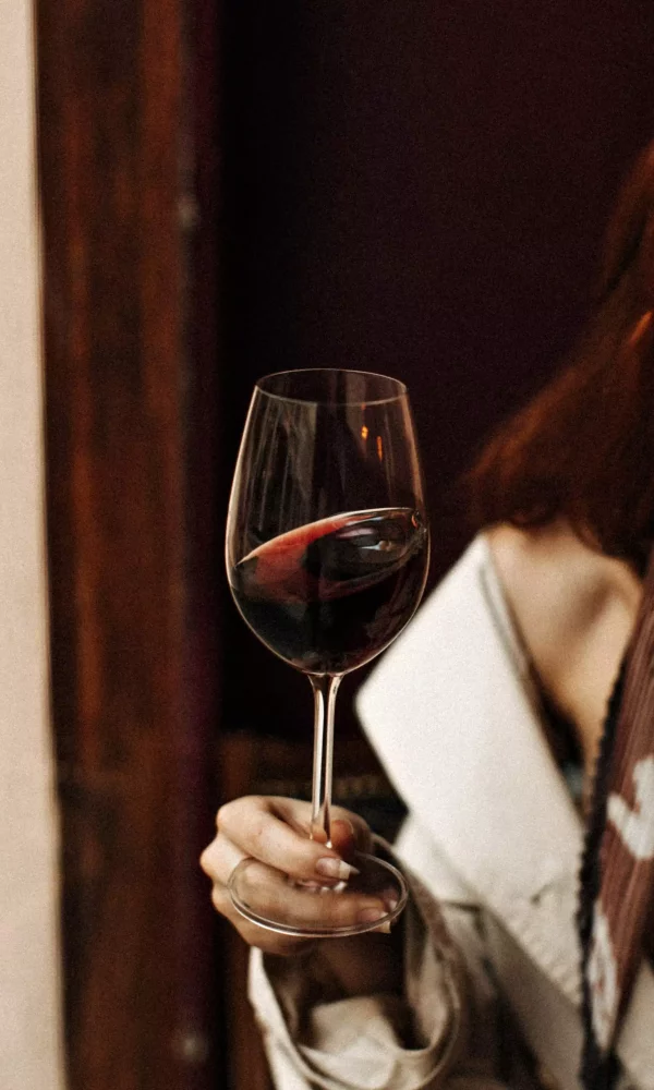 Snapshot of wine glass. Red-haired woman in white dress poses with alcohol in bar